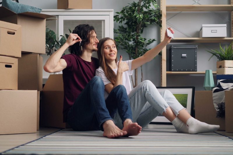 Young couple sitting among moving boxes taking a selfie cele 1791306358